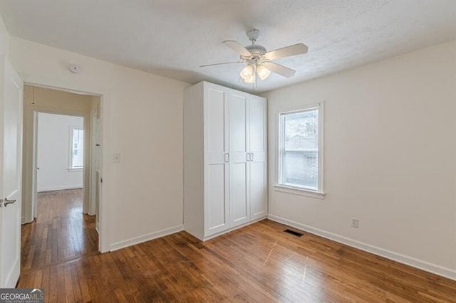 unfurnished bedroom featuring wood finished floors, baseboards, a closet, and ceiling fan