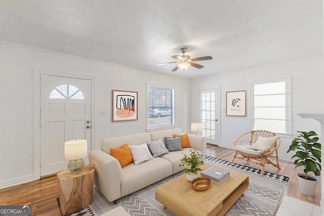 living room with a ceiling fan, healthy amount of natural light, wood finished floors, crown molding, and baseboards
