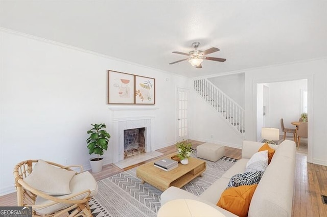 living area with stairs, ornamental molding, wood finished floors, a fireplace with flush hearth, and ceiling fan