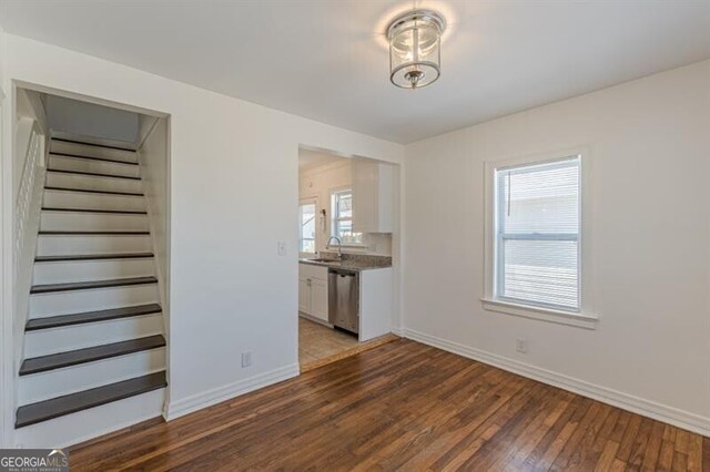 unfurnished living room with stairs, hardwood / wood-style flooring, baseboards, and a sink