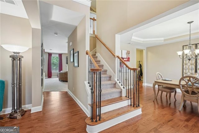 6565 Bentley Ridge Dr, Cumming, GA 30040 - staircase featuring wood finished floors, a chandelier, and a tray ceiling