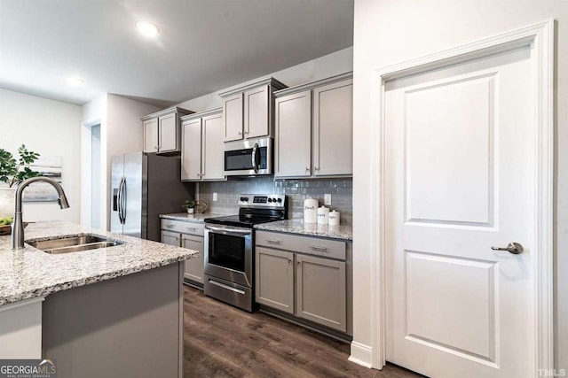 kitchen with a sink, decorative backsplash, gray cabinets, appliances with stainless steel finishes, and dark wood-type flooring