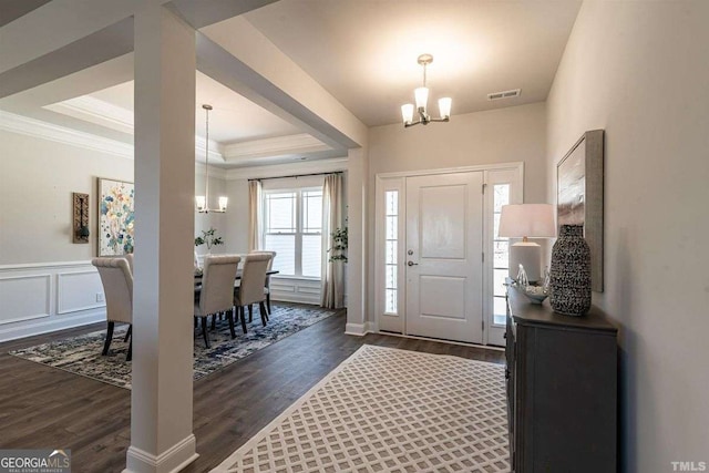 entryway with a raised ceiling, visible vents, dark wood-type flooring, crown molding, and a notable chandelier