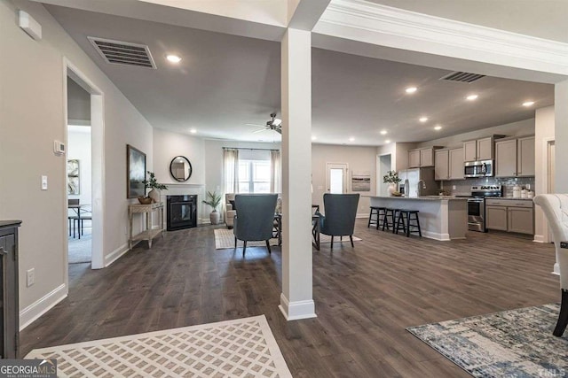 living room featuring dark wood finished floors, visible vents, baseboards, a glass covered fireplace, and ceiling fan