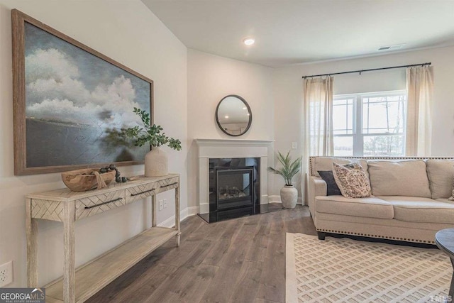 living area with visible vents, a glass covered fireplace, baseboards, recessed lighting, and wood finished floors