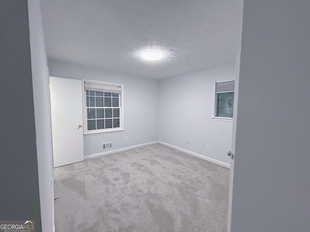 carpeted spare room featuring a textured ceiling, visible vents, and baseboards