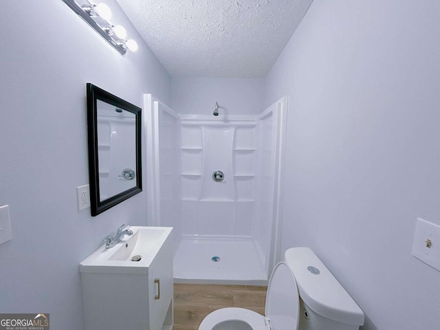 bathroom with a shower stall, wood finished floors, toilet, vanity, and a textured ceiling