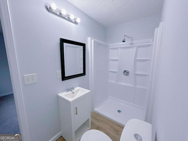 full bath featuring a textured ceiling, toilet, walk in shower, wood finished floors, and vanity