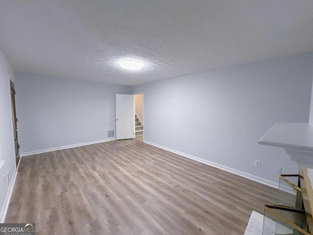 unfurnished living room with visible vents, baseboards, wood finished floors, and stairs