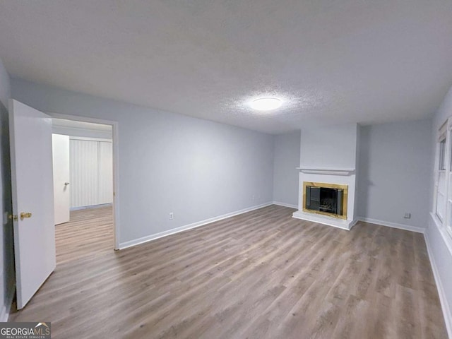 unfurnished living room featuring baseboards, a glass covered fireplace, wood finished floors, and a textured ceiling