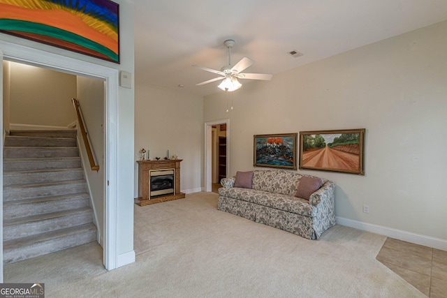 carpeted living area featuring a ceiling fan, stairs, a glass covered fireplace, baseboards, and visible vents