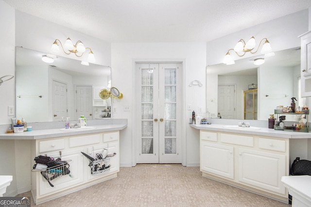 bathroom with french doors, two vanities, and a stall shower
