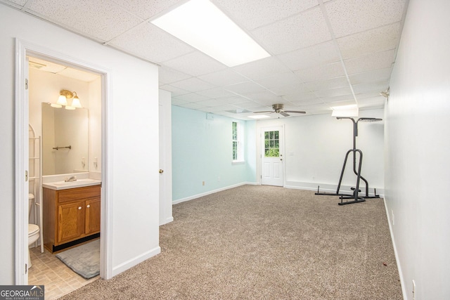 below grade area with ceiling fan, a drop ceiling, light carpet, baseboards, and a sink