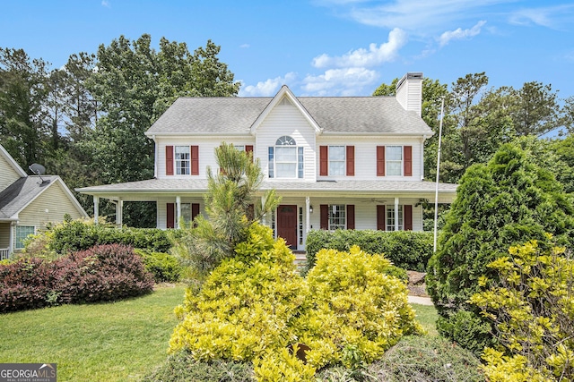 colonial house featuring a chimney, a porch, a front lawn, and a shingled roof
