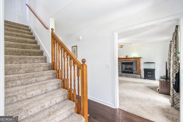 staircase with a brick fireplace, wood-type flooring, and baseboards