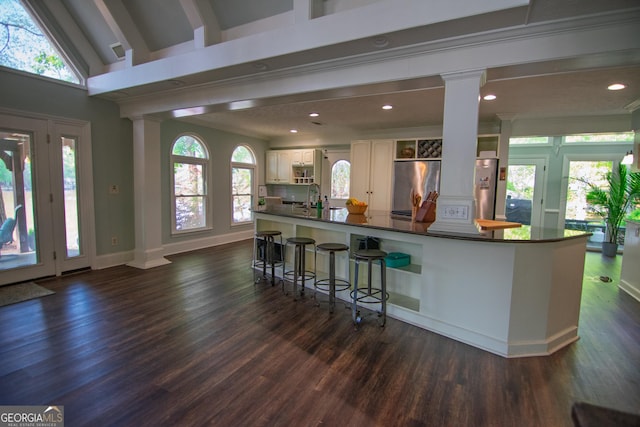 kitchen with dark countertops, stainless steel refrigerator, a sink, dark wood-type flooring, and decorative columns