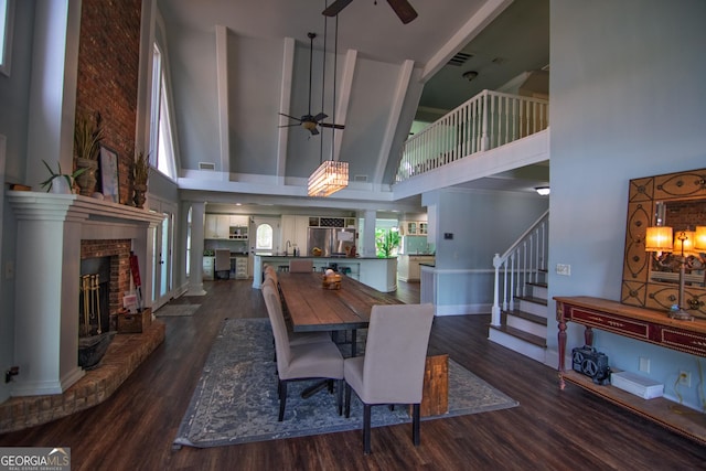 dining room with visible vents, a towering ceiling, ceiling fan, a fireplace, and dark wood-type flooring