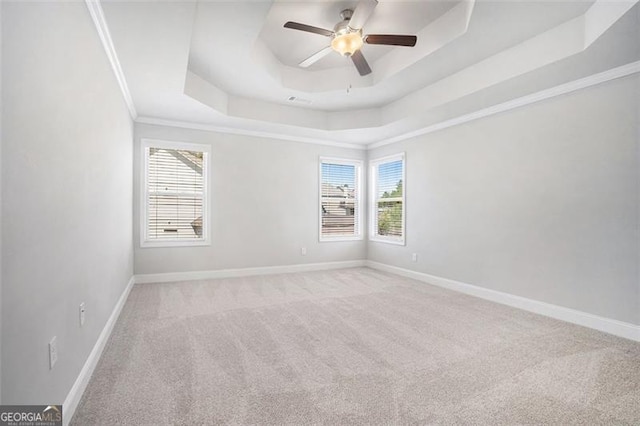 carpeted spare room featuring a tray ceiling, crown molding, a ceiling fan, and baseboards