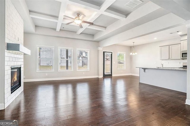 unfurnished living room with visible vents, dark wood-type flooring, beamed ceiling, a large fireplace, and ceiling fan with notable chandelier