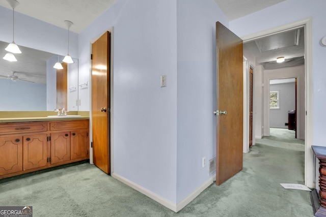 hallway with light colored carpet, a sink, attic access, and baseboards