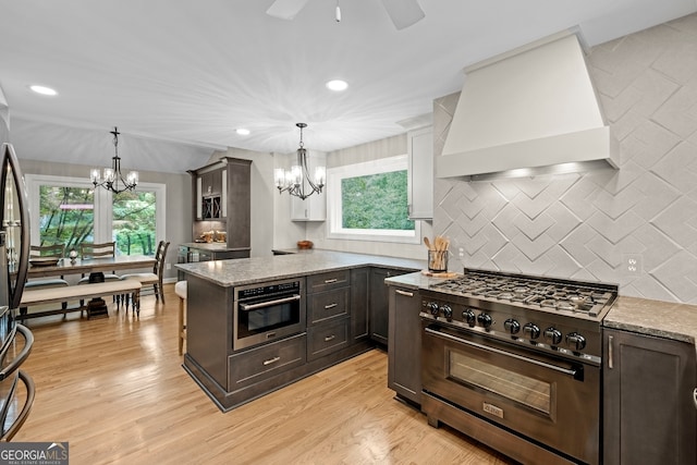 kitchen featuring light stone counters, stainless steel appliances, backsplash, light wood-type flooring, and wall chimney exhaust hood