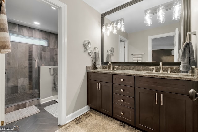 bathroom with baseboards, a shower stall, double vanity, and a sink