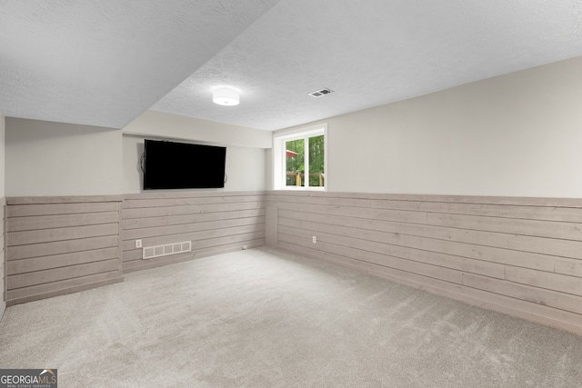 basement featuring carpet flooring, wooden walls, a textured ceiling, and visible vents