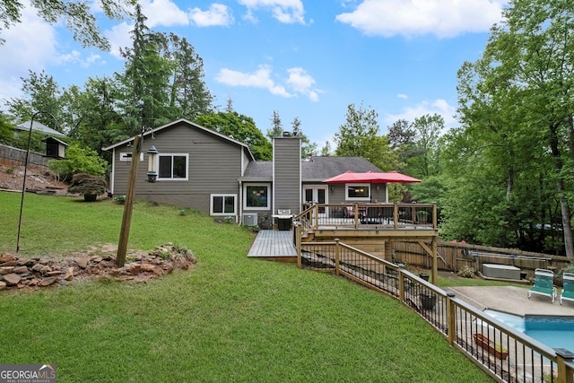 rear view of property with a deck, a chimney, a fenced backyard, a fenced in pool, and a lawn