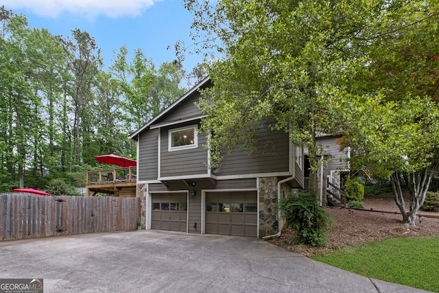 view of side of property featuring aphalt driveway, stone siding, a deck, fence, and a garage