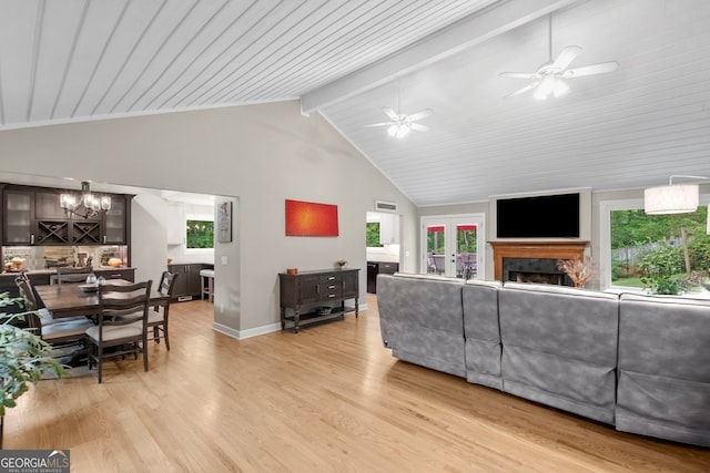 living area featuring ceiling fan with notable chandelier, light wood finished floors, a fireplace, baseboards, and high vaulted ceiling