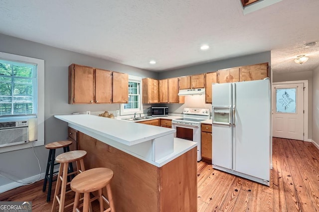 kitchen with a sink, under cabinet range hood, light wood-type flooring, a peninsula, and white appliances