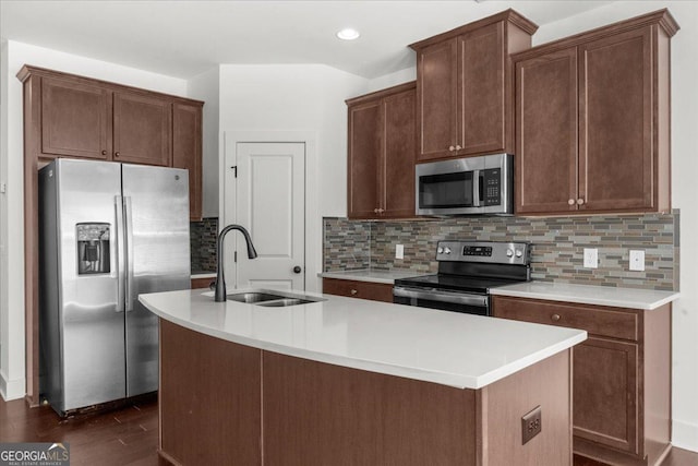 kitchen with a sink, a kitchen island with sink, appliances with stainless steel finishes, light countertops, and dark wood-style flooring