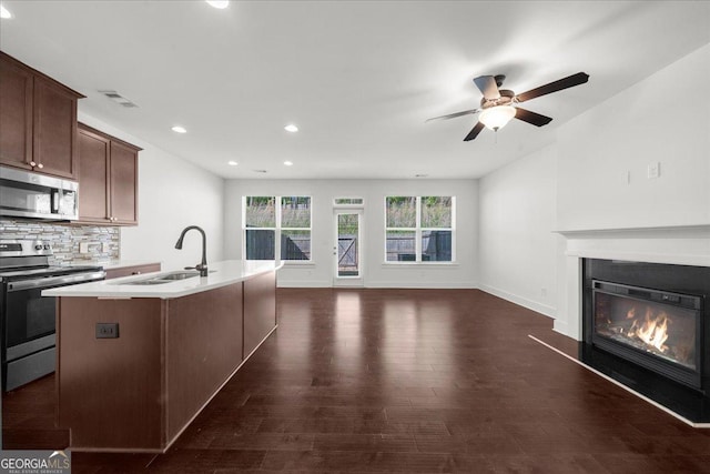 kitchen with a sink, a glass covered fireplace, ceiling fan, light countertops, and appliances with stainless steel finishes