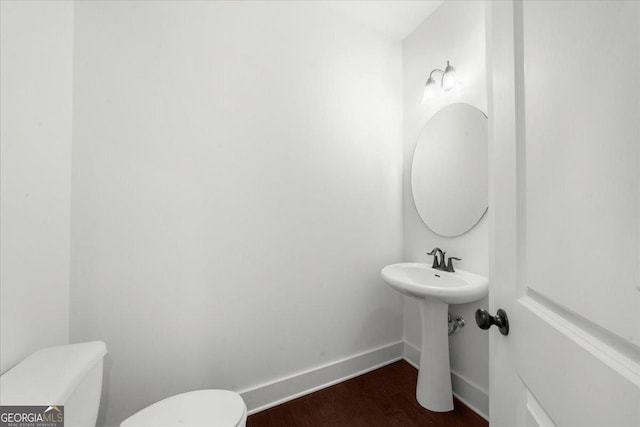 half bath featuring a sink, toilet, wood finished floors, and baseboards