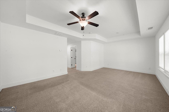 unfurnished room with light colored carpet, ceiling fan, visible vents, and a raised ceiling