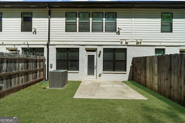 rear view of house with a fenced backyard, central AC unit, brick siding, a yard, and a patio