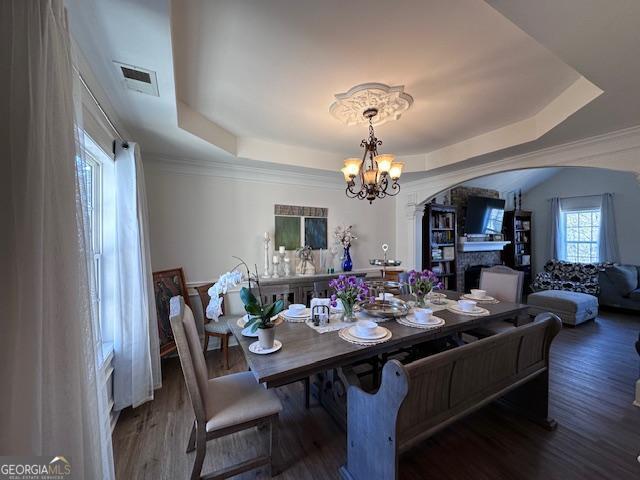 dining room featuring arched walkways, a raised ceiling, a chandelier, and wood finished floors