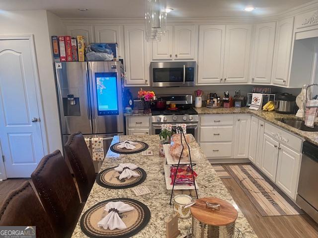 kitchen with appliances with stainless steel finishes, white cabinetry, light stone countertops, and a sink