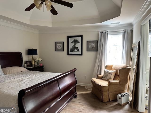 bedroom featuring wood finished floors, a tray ceiling, ornamental molding, a ceiling fan, and baseboards