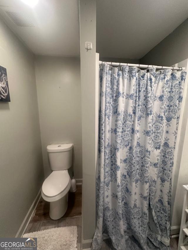bathroom with wood finished floors, toilet, baseboards, and a shower with curtain