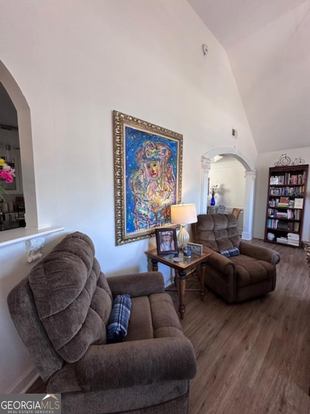 living room featuring arched walkways, wood finished floors, high vaulted ceiling, and baseboards