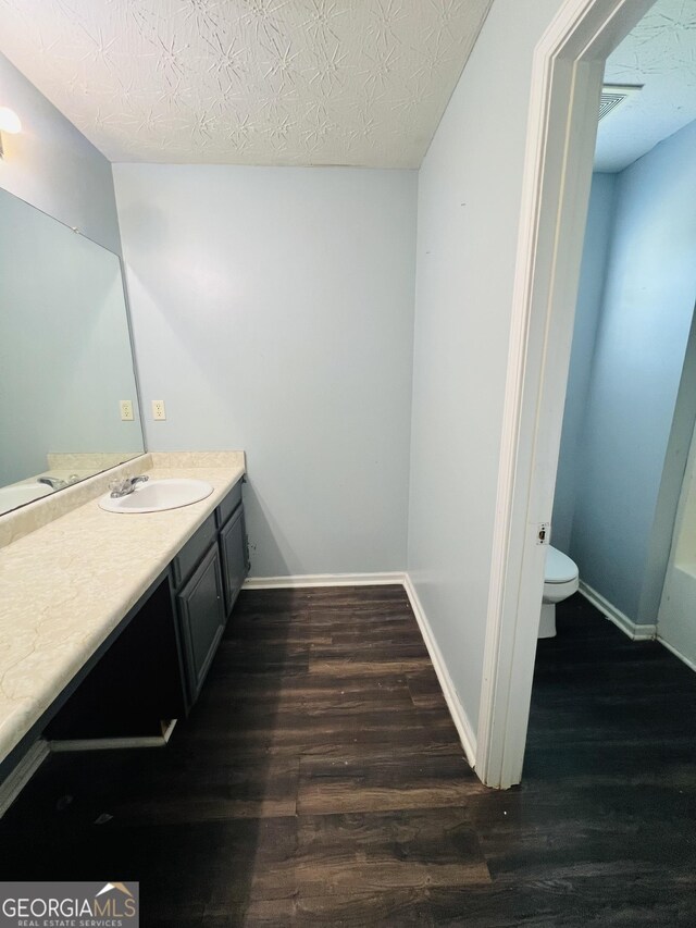 bathroom featuring toilet, vanity, wood finished floors, and a textured ceiling
