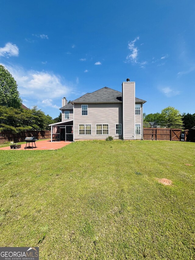 rear view of house with a chimney, fence, a yard, a patio area, and a sunroom