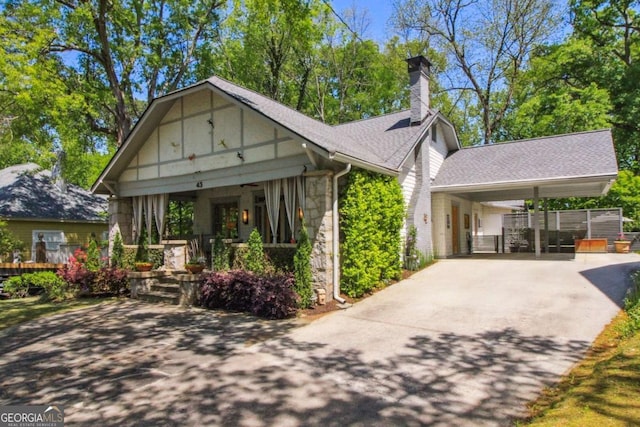 view of front of home with concrete driveway, a chimney, stone siding, a shingled roof, and an attached carport
