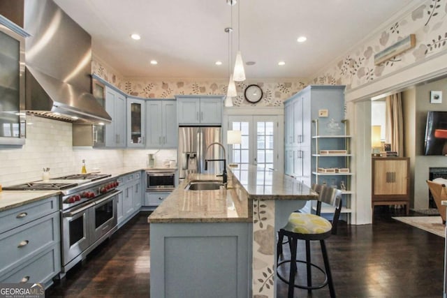 kitchen featuring french doors, a sink, gray cabinetry, wall chimney range hood, and appliances with stainless steel finishes