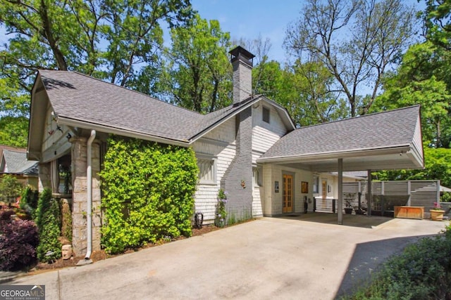 view of front of property featuring driveway, a shingled roof, a chimney, and a carport