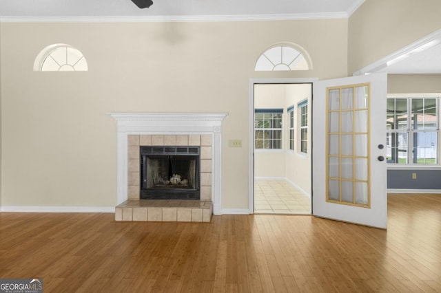 unfurnished living room featuring wood-type flooring, a tile fireplace, crown molding, and baseboards