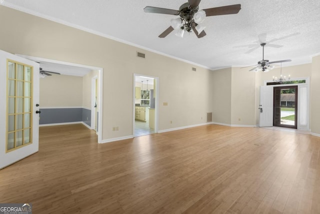 unfurnished living room with ceiling fan with notable chandelier, plenty of natural light, wood finished floors, and visible vents