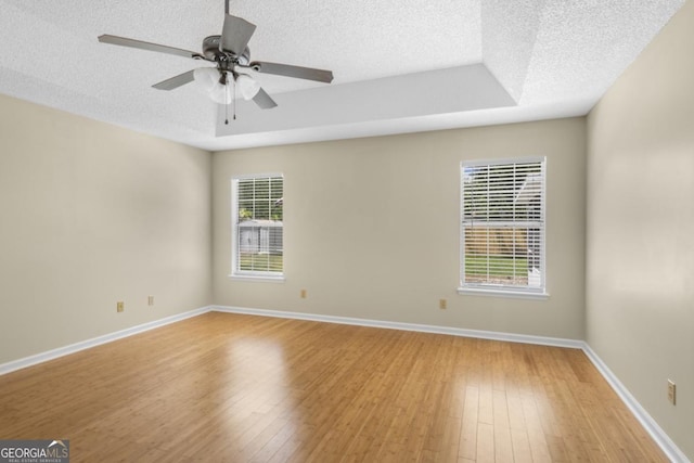 spare room with a tray ceiling, a ceiling fan, baseboards, light wood-style flooring, and a textured ceiling