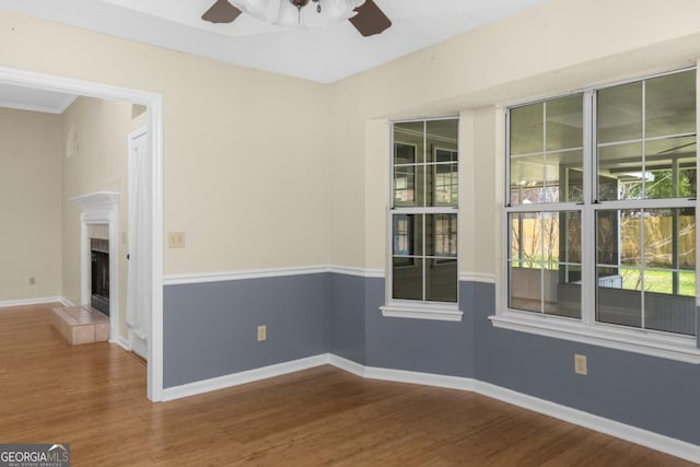 spare room with wood finished floors, a tiled fireplace, a ceiling fan, and baseboards